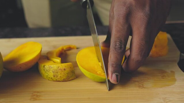 Closeup of male hands cutting mango fruit with a knife on a wooden board