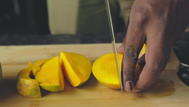 Closeup of male hands cutting mango fruit with a knife on a wooden board