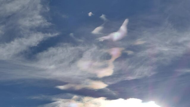 Natural blue sky and colorful decorative clouds moving very slowly - Cloud iridescence, irisation around sun. Sunny autumn calm sky with colorful pearl colors - optical phenomenon.