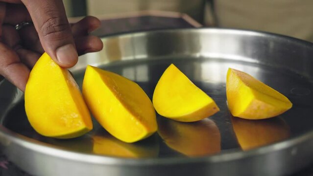 A closeup of cut or sliced juicy mango pieces picked from a steel plate