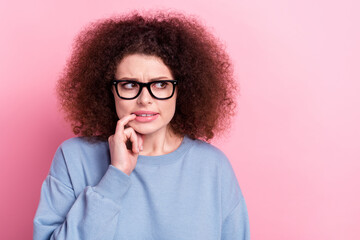 Portrait of nervous curly hairdo girl wear blue sweatshirt bite nail looking empty space worried her boss abuse isolated on pink background