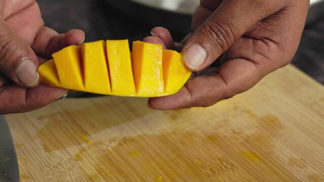 Closeup of male hands dicing a mango slice on a wooden chopping board