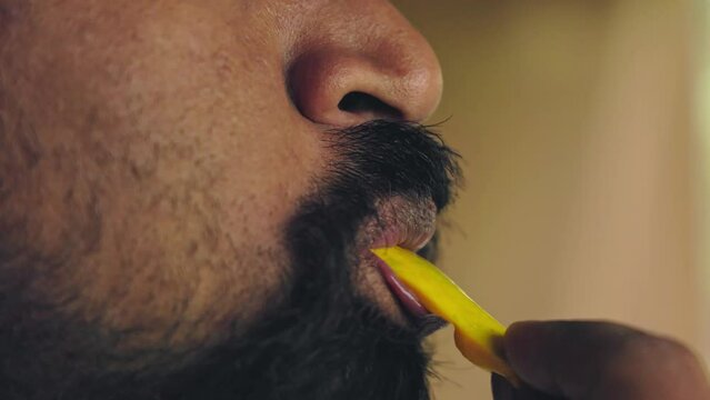 A bearded man savors the mango slice by enjoying it through sucking or eating