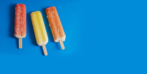 three colorful fruit ice-cream popsicles over blue background with copy space 