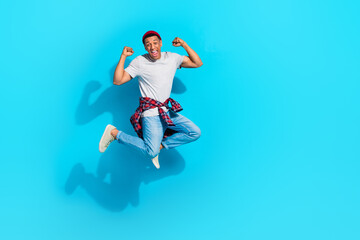 Fototapeta na wymiar Full size photo of delighted excited man jumping raise fists achieve triumph empty space isolated on blue color background