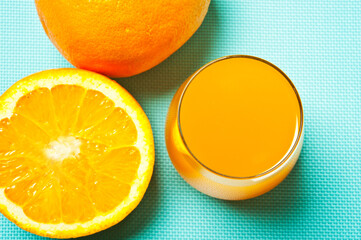 a glass of  orange juice with half orange and whole citrus a aquamarine background and copy space