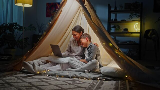 Mom and son have video call on laptop, sitting inside game tent at home. People. Technology. Family
