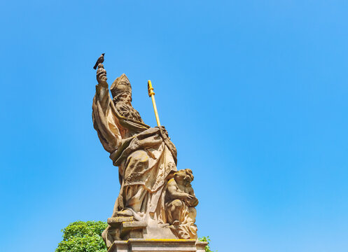 Old statue of st. Augustine of Hippo and gray crow on Charles Bridge in Prague, Czech Republic