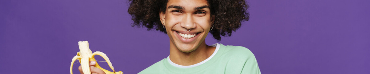 Young smiling handsome latin man holding bitened banana in hand