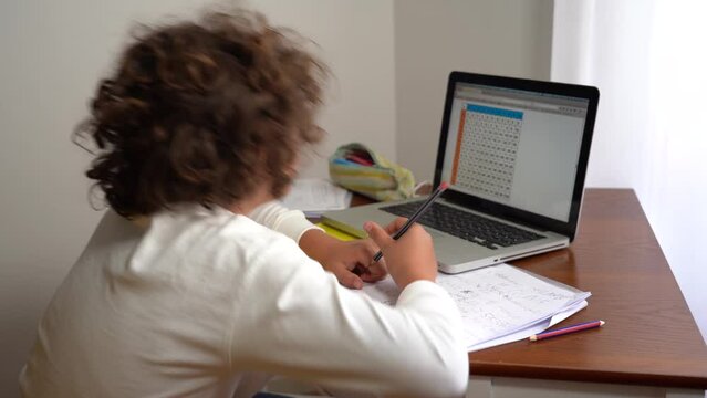 9-year-old elementary school boy doing homework - doing school-given math exercises for the summer holidays - childhood lifestyle student with computer laptop 
