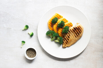 Healthy food grilled chicken has broccoli pumpkin vegetable in plate on white wood table.