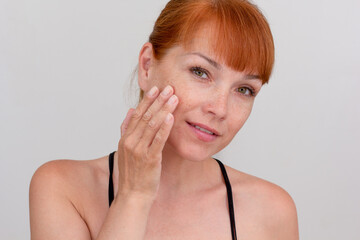 Portrait of cropped caucasian middle aged woman face with freckles touching skin by hand on white background looking at camera