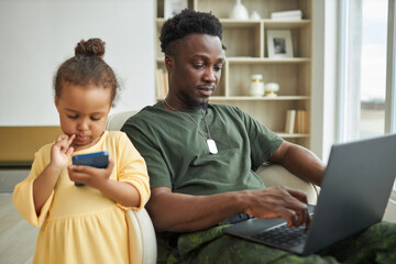 African American dad in military uniform working online on laptop while sitting with child at home