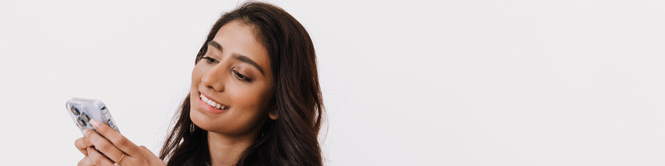 Obraz premium Young brunette indian woman smiling while using cellphone