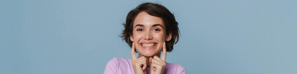 White excited woman wearing t-shirt pointing fingers at her cheek