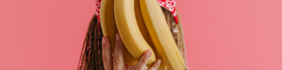 White woman with dreadlocks showing bananas at camera