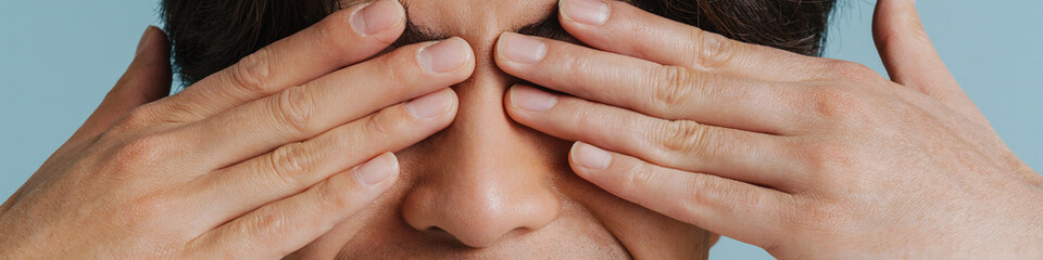 Young handsome smiling asian boy covering his eyes with hands