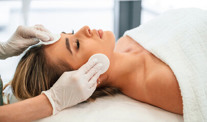 Cleaning skin by using cotton pad or sponge. Woman face getting facial care by beautician hands at spa salon © standret