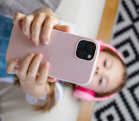 Child in headphones with mobile smart phone in hands makes photo. Top view