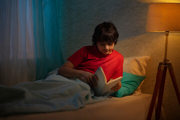 Little boy reading a book while lying on bed