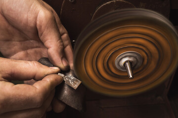 Jeweler polishes a silver pendant in the form of an icon on a machine tool in a workshop