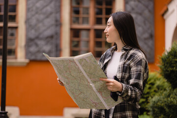 Portrait of a beautiful happy brunette Korean woman holding a map on the streets of the old city. Asian woman tourist lady traveling in Europe.