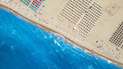 The coastline of the sea with a sandy clean beach and colored umbrellas is located diagonally across the frame. Shooting from a drone