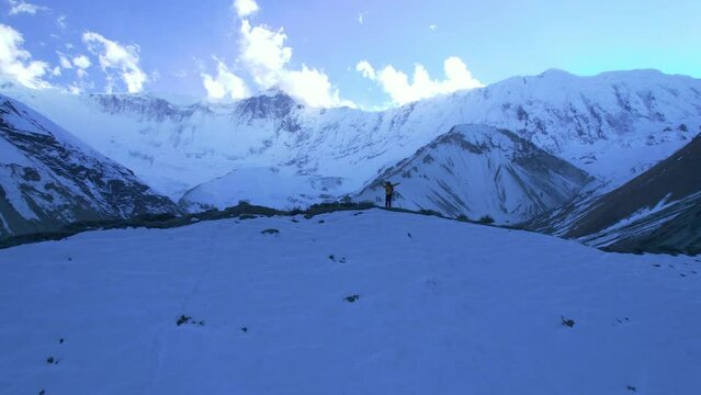 Aerial circular view male hiker in yellow jacket on hilltop raising hands arms up to the sky enjoy reaching goals. Travels and hiking outdoors, trekking in Himalaya, Asia, Tilicho