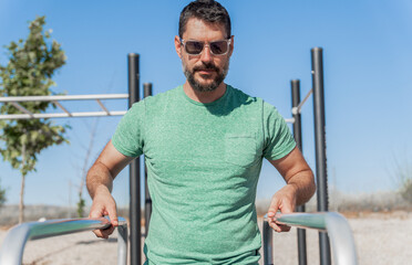 man with beard and sunglasses training his arms on parallel bars in a park gymn