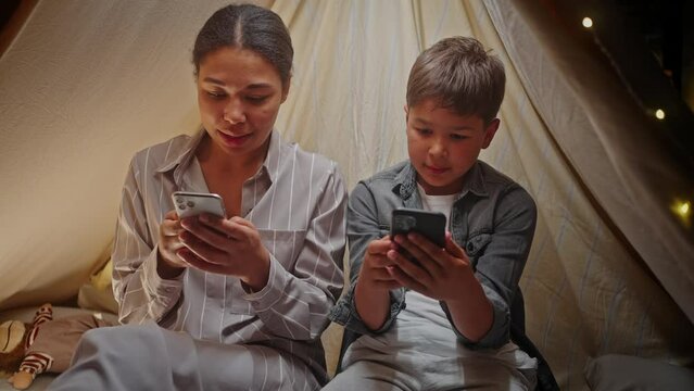 Mother and son using smartphone, playing video games, checking social media content in a play tent