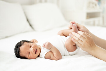 mom's hands of a white-skinned woman gently stroke the tummy or massage a newborn African-American baby, a small child lies on the bed in the bedroom after waking up or falling asleep