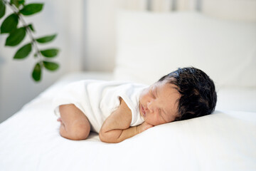 Obraz na płótnie Canvas a newborn black African-American baby is sleeping sweetly on his tummy, a small dark-skinned baby is lying on the bed in the bedroom in close-up