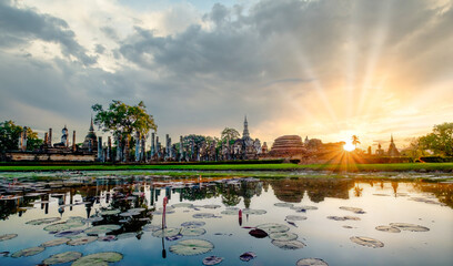 Sunset over Wat Mahathat Buddhist temple in Sukhothai historical park with dramatic sky and clouds.