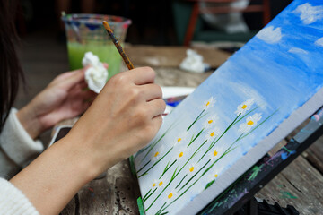 Close-up small paintbrush with yellow paint on paintbrush, painter's hand holding handle firmly, dip into center where there is white flower petal that is daisy, poke slowly make it look beautiful.
