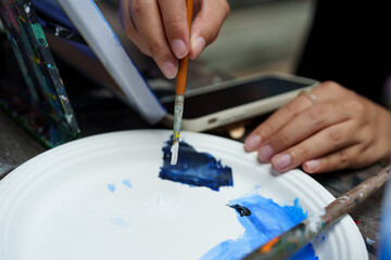 Beautiful Asian woman with, sitting using long-handled brush beautiful, paint blue on piece cloth that intends depict bright sky, paint back forth left right spread color evenly across fabric.