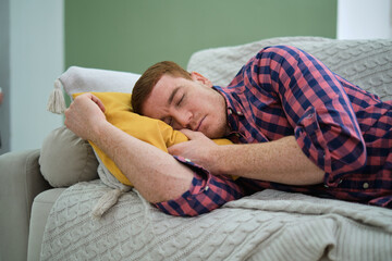 exhausted man in shirt and jeans is overcome by fatigue and drifts off into a daytime nap on his...
