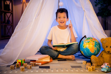 Photo of excited inspired schoolkid prepare homework geography read interesting facts earth in textbook diy camp nursery playroom