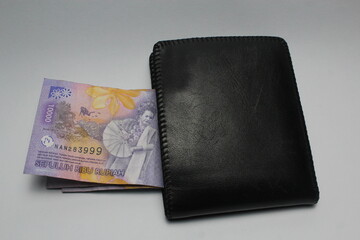 Black leather wallet and ten thousand rupiah note on a white background