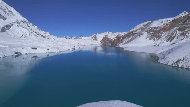 Aerial birds eye view panning view blue alpine Tilicho lake surrounded by snowy Himalayas mountains in Nepal. Manang district. Considered highest Alpine lake in the world