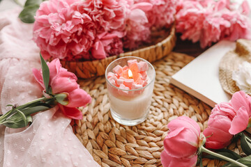 Cozy spring composition, burning candle, peonies and hat.
