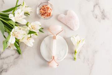 A professional rose quartz massager for facial care at home lies on a white marble round podium...
