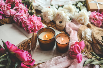 Two burning candles and pink peonies, spring atmosphere
