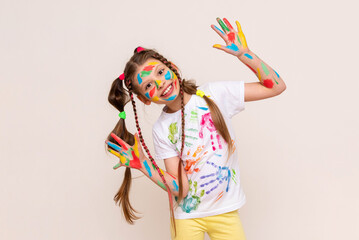 A little schoolgirl with painted hands and face with multicolored paints. A girl stained with paints. The concept of children's creativity. Funny child draws with his hands.