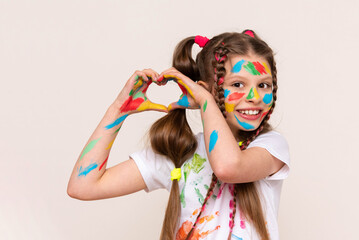 A little schoolgirl with painted hands and face with multicolored paints. A girl stained with...