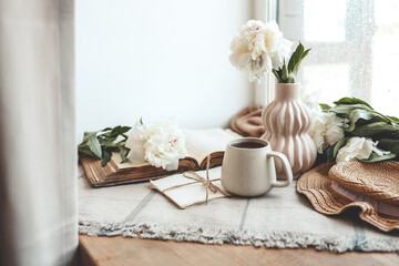 Cup of tea, straw hat, open book and peonies, spring still life