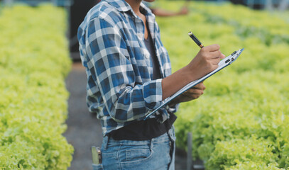 Female scientist examining a plants in greenhouse farm. scientists holding equipment for research plant in organic farm. Quality control for hydroponics vegetable farm.