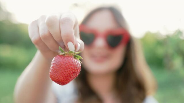 Young woman with red ripe strawberry on green garden background.Positive footage