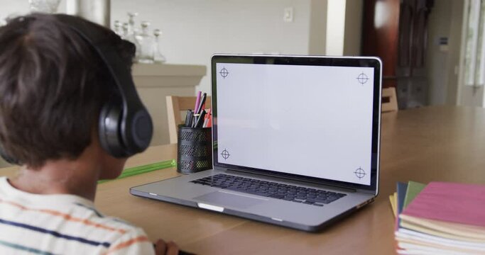 Biracial boy learning online at table using laptop with copy space on screen, slow motion