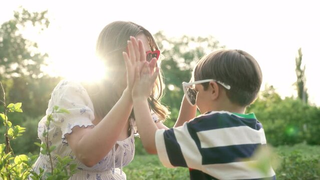 Beautiful smiling mother gives little son high five on sunset garden background.