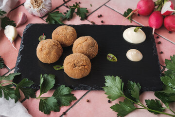homemade fried mushroom meatballs with sauce on black stone background, pink table tiles, fresh herbs and ingredients